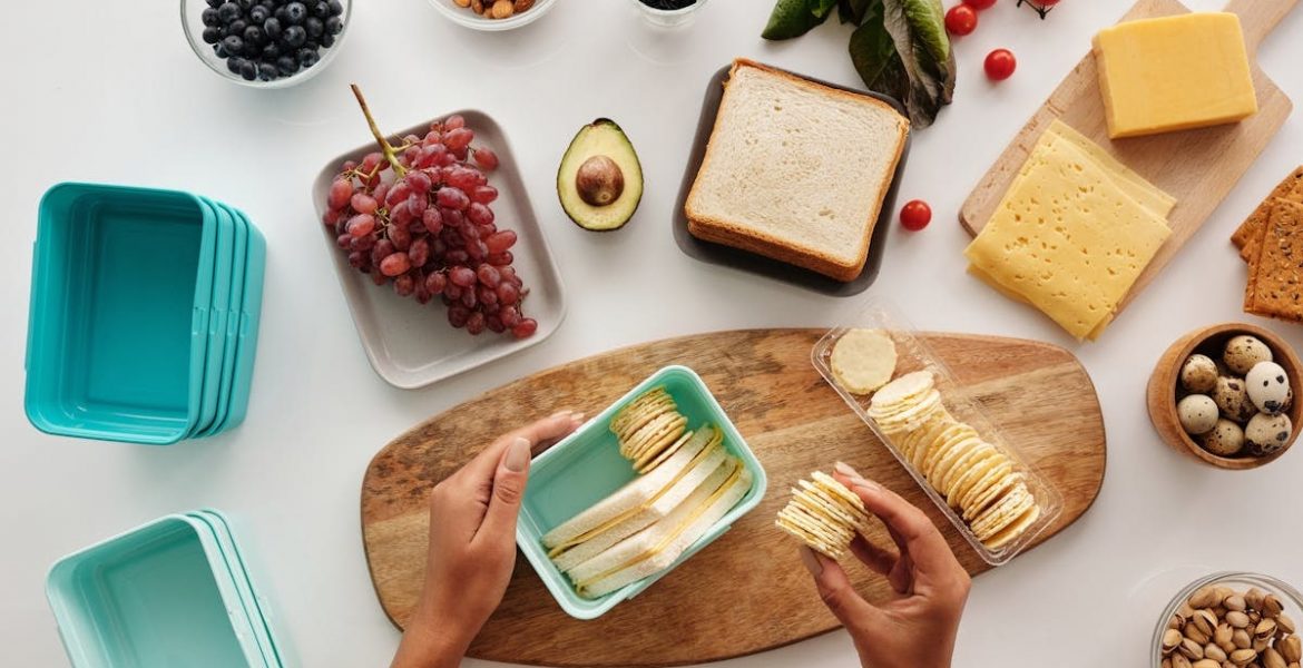 Top view of preparing a healthy lunch with fruits, cheese, and crackers, showcasing fresh ingredients and a vibrant lifestyle.