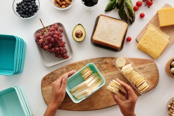 Top view of preparing a healthy lunch with fruits, cheese, and crackers, showcasing fresh ingredients and a vibrant lifestyle.