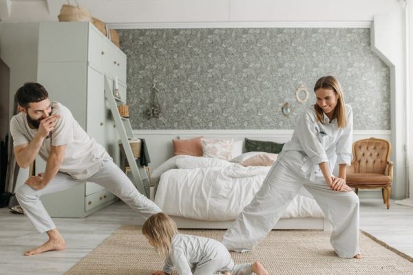 A joyful family bonding through morning stretches in a cozy bedroom setting.