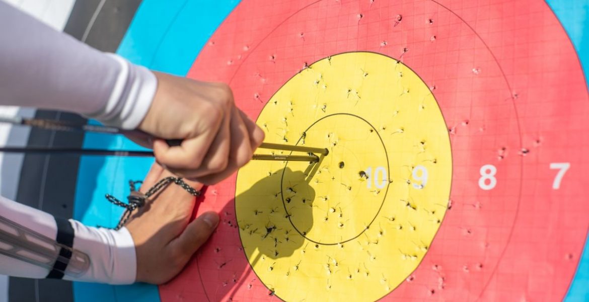 An archer retrieves arrows from a colorful archery target during a sunny day outdoors.